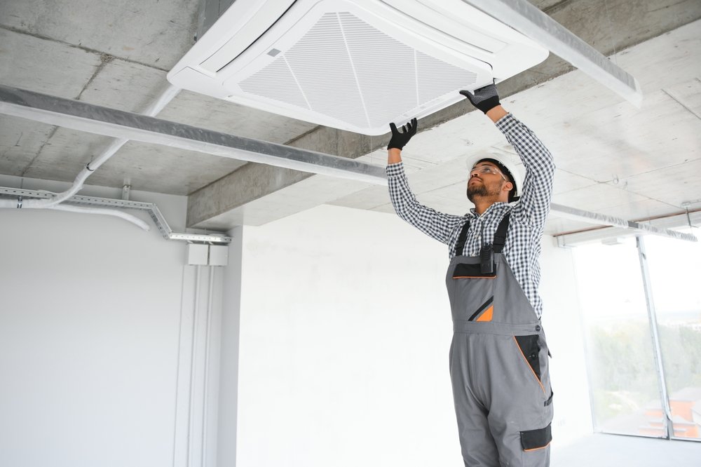 A technician installing or servicing a ceiling-mounted air conditioning unit in a modern industrial-style building.
