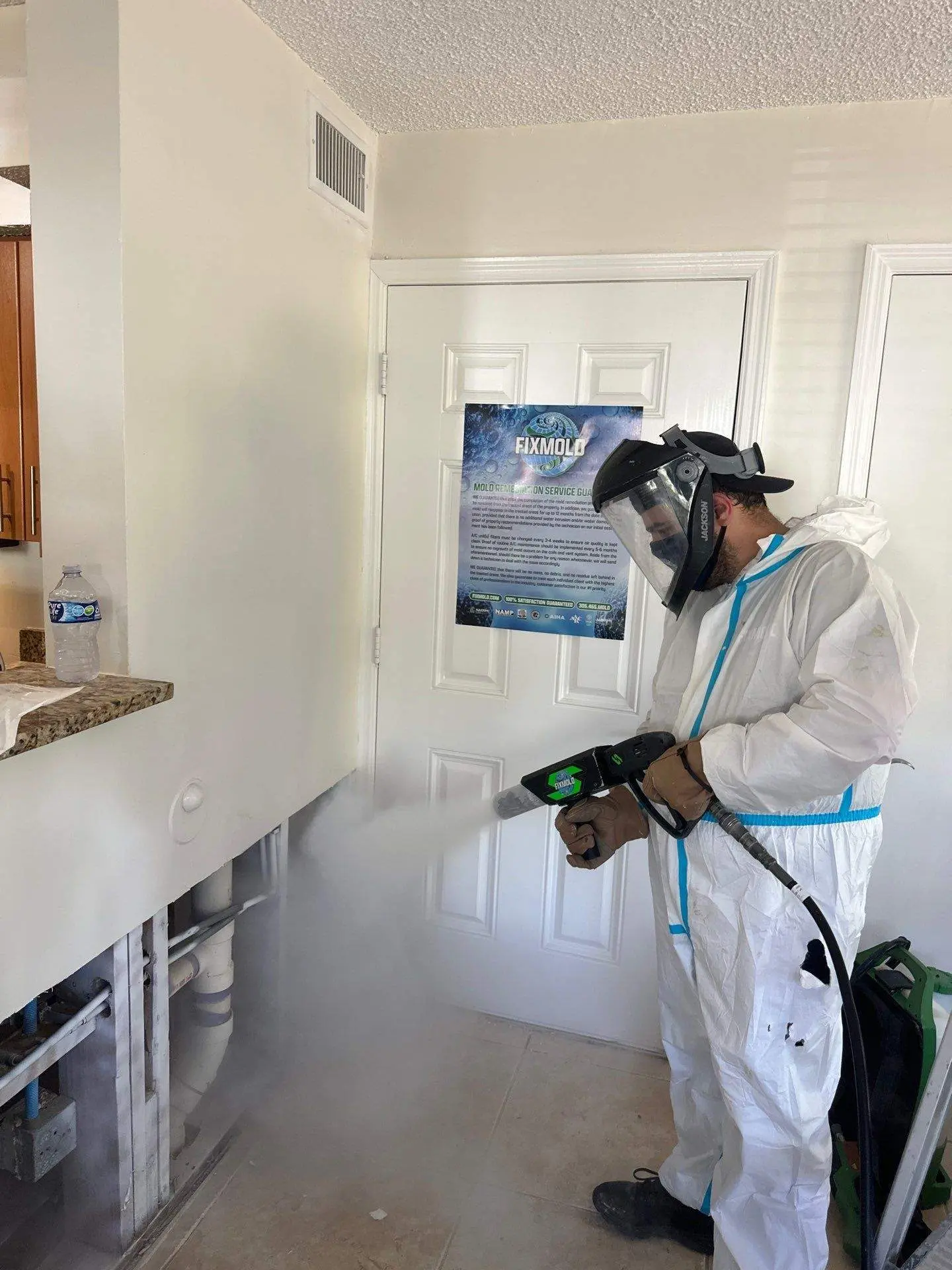 A technician in a white hazmat suit performs mold remediation inside a damaged interior space