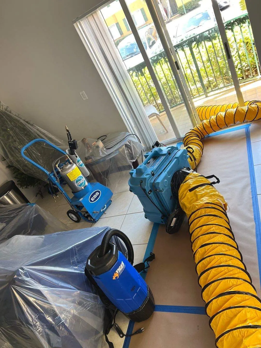 Residential mold mitigation setup with protected furniture, air movers, and yellow ventilation hoses