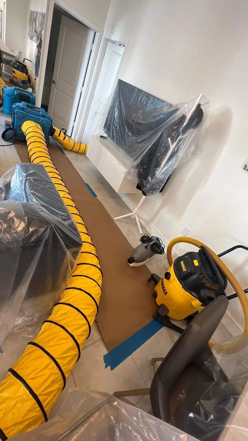 Residential mold drying setup with fans, hoses, and furniture covered in plastic